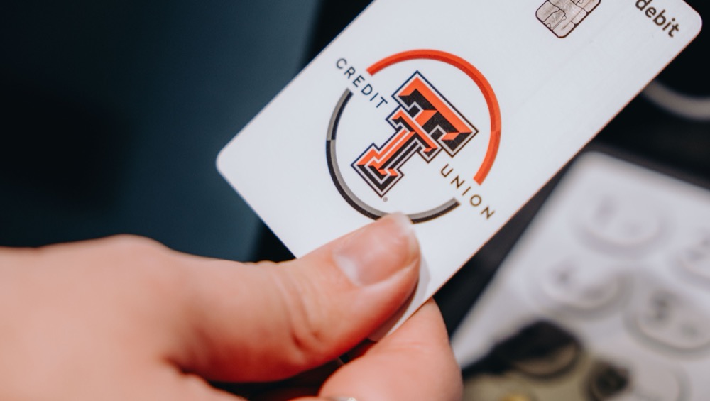Hand holding a Texas Tech Credit Union debit card over a payment terminal
