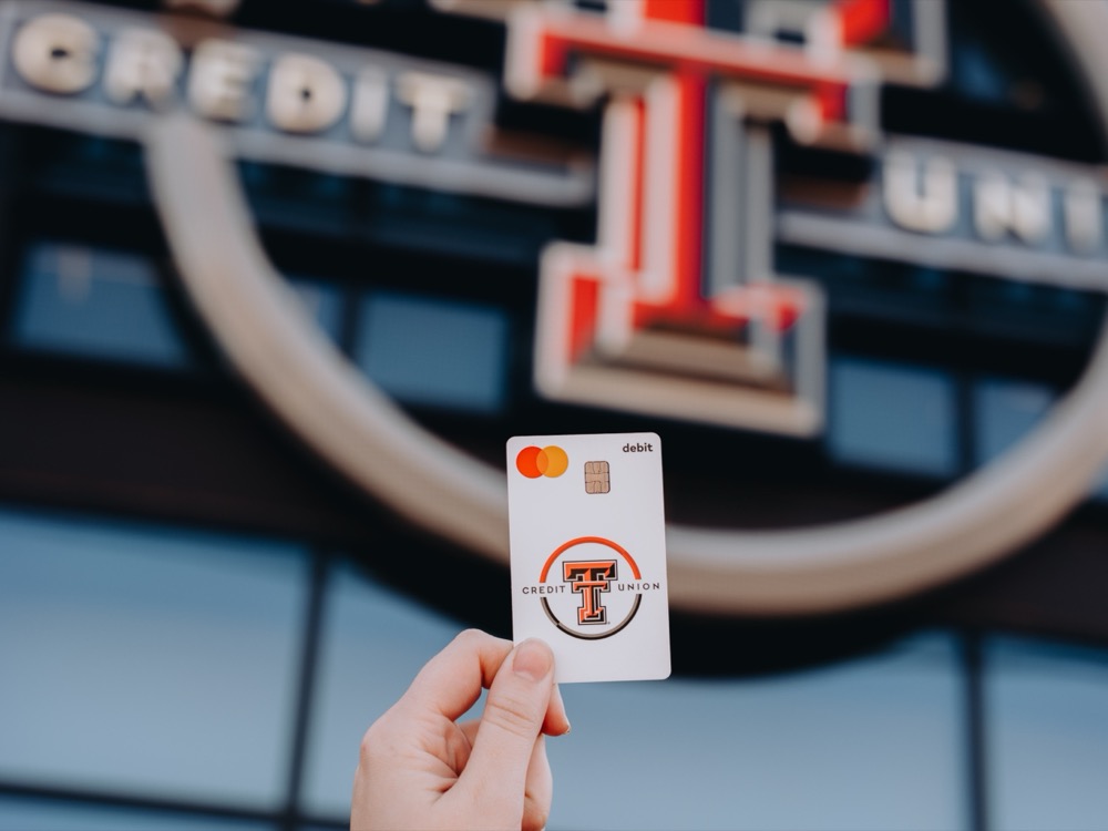 Hand holding a Texas Tech Credit Union debit card in front of the Double T sign